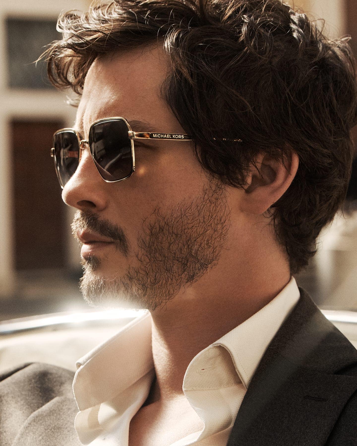 Logan Lerman wearing dark oversized sunglasses and white collared shirt for Michael Kors campaign