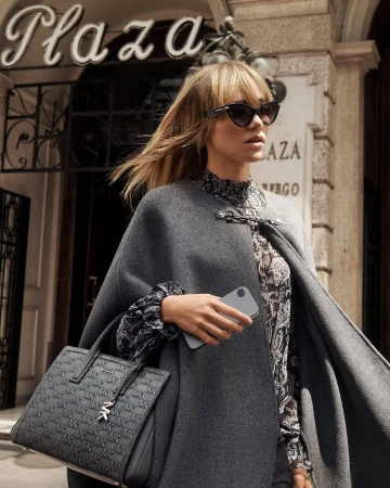 Model Suki Waterhouse in a grey cape holding a patterned handbag outside the Grand Hotel Plaza in Rome.
