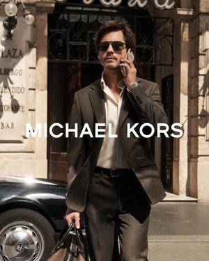 Logan Lerman in a dark suit jacket holding a phone outside Grand Hotel Plaza in Rome for Michael Kors