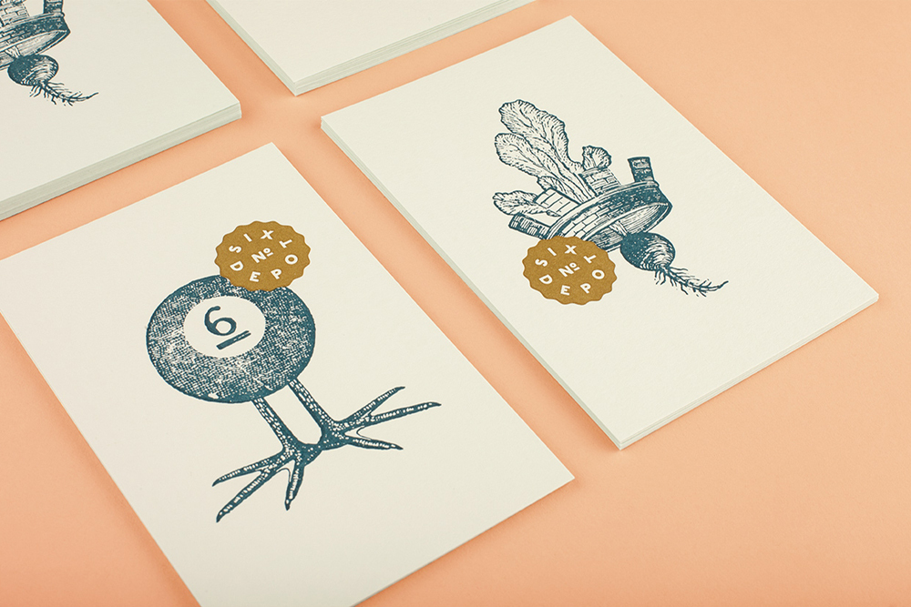 Printed paper cards featuring blue engraved illustrations and gold seal logo stickers on peach surface