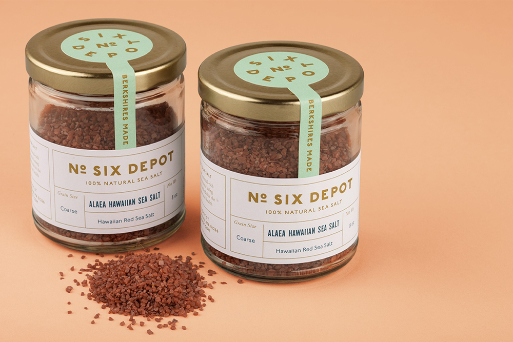 Two glass jars of Hawaiian sea salt with gold lids and mint green labels on a peach background