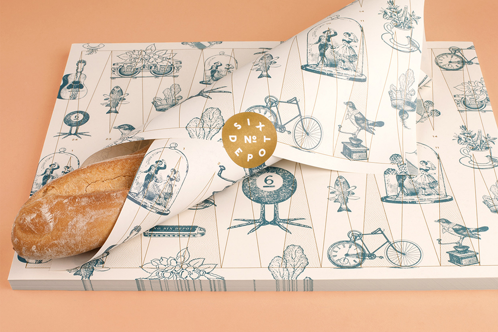 Baguette wrapped in patterned paper with blue illustrations and a gold circular seal for No. Six Depot