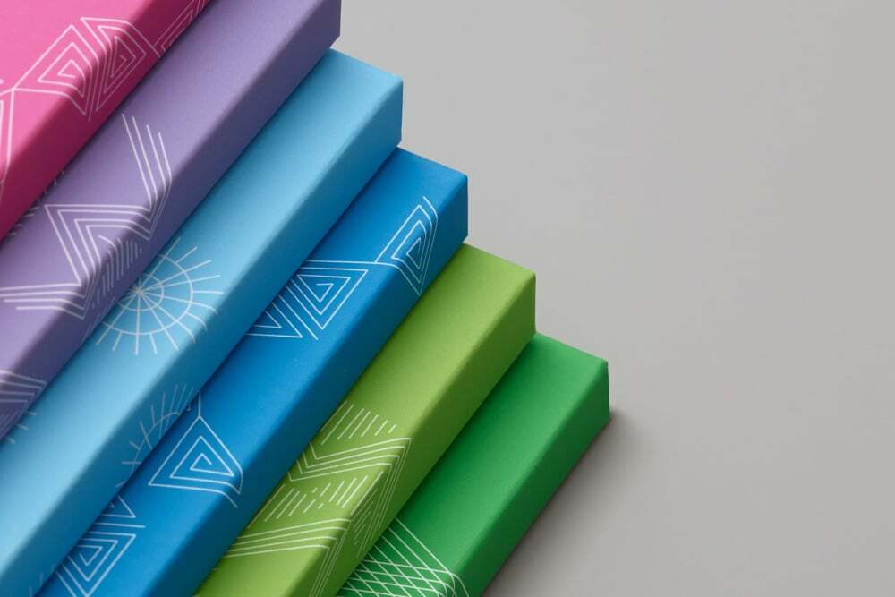 Stacked colorful rectangular boxes with white geometric line patterns on a neutral grey background.