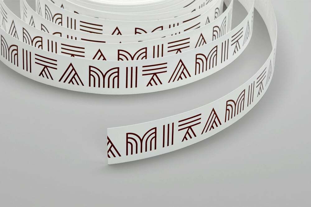 White ribbon printed with repeated brown geometric brand patterns and typography on a seamless light background