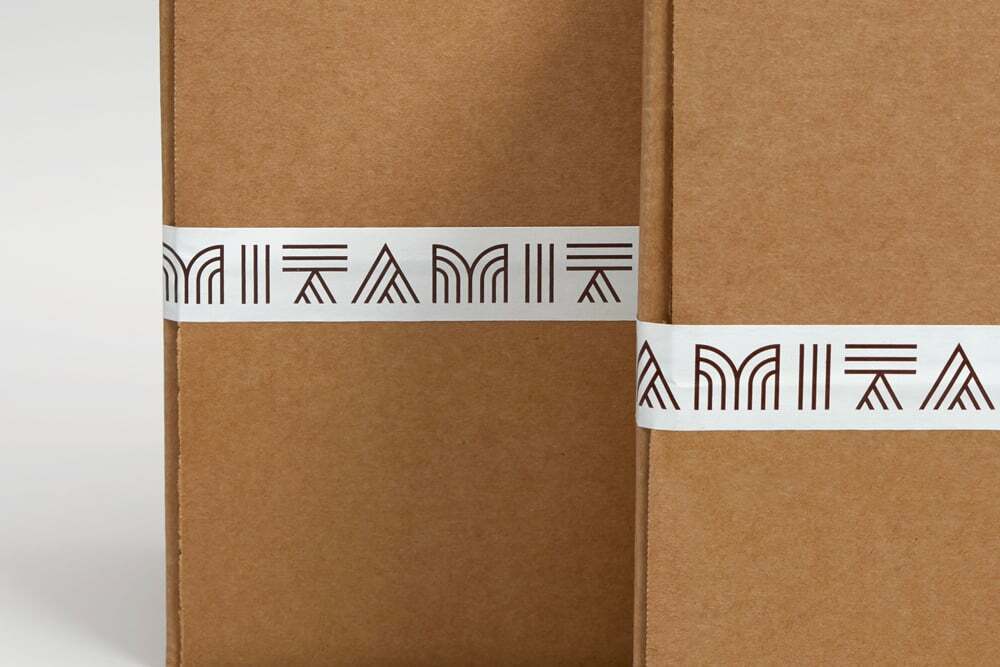 Close-up product shot of brown kraft cardboard packaging boxes secured with branded white belly bands featuring repeated geometric typography.
