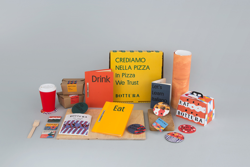 Bottura brand identity packaging collection including yellow pizza box, notebooks, cup, coasters, and patterned food boxes