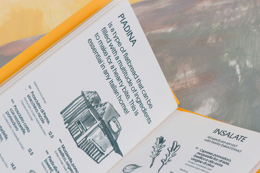 Open menu book with typographic layout and black ink spot illustrations on white paper against a painted yellow background