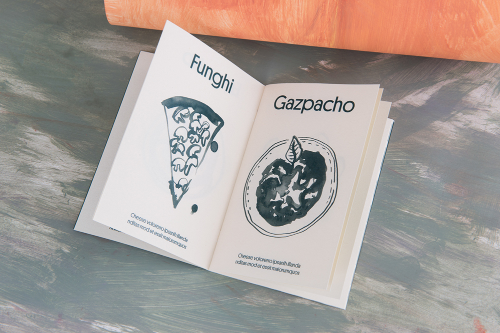 An open book with illustrated food items and typography resting on a textured wooden surface.