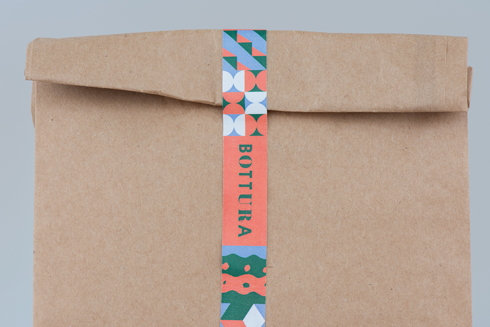 Brown paper bag sealed with a colourful patterned label bearing the Bottura brand name against a light grey background.