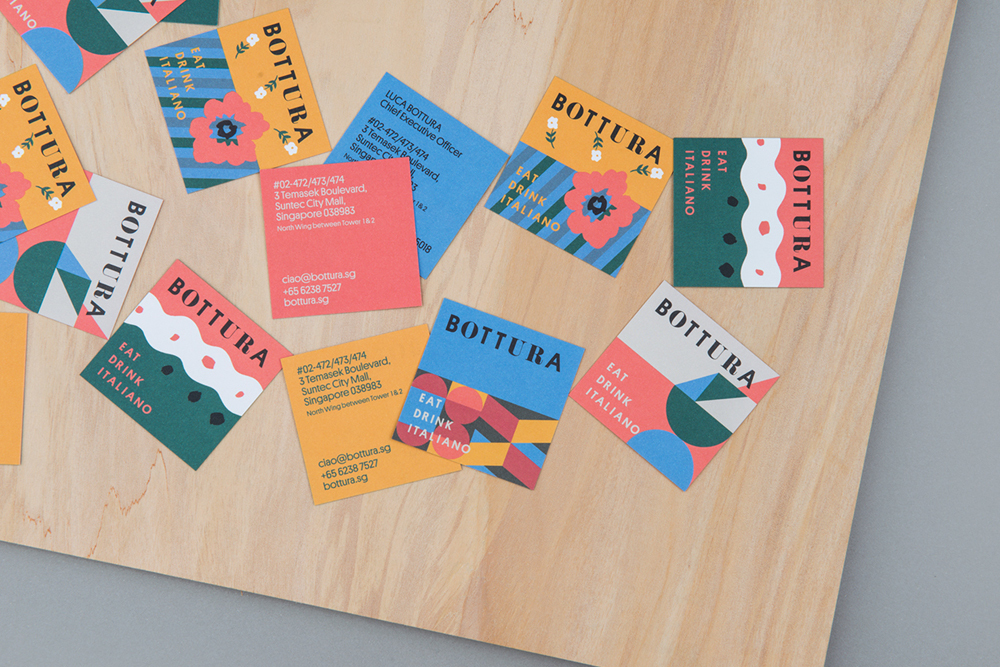 Collection of colorful branded business cards scattered across a light wooden surface for Bottura brand identity.