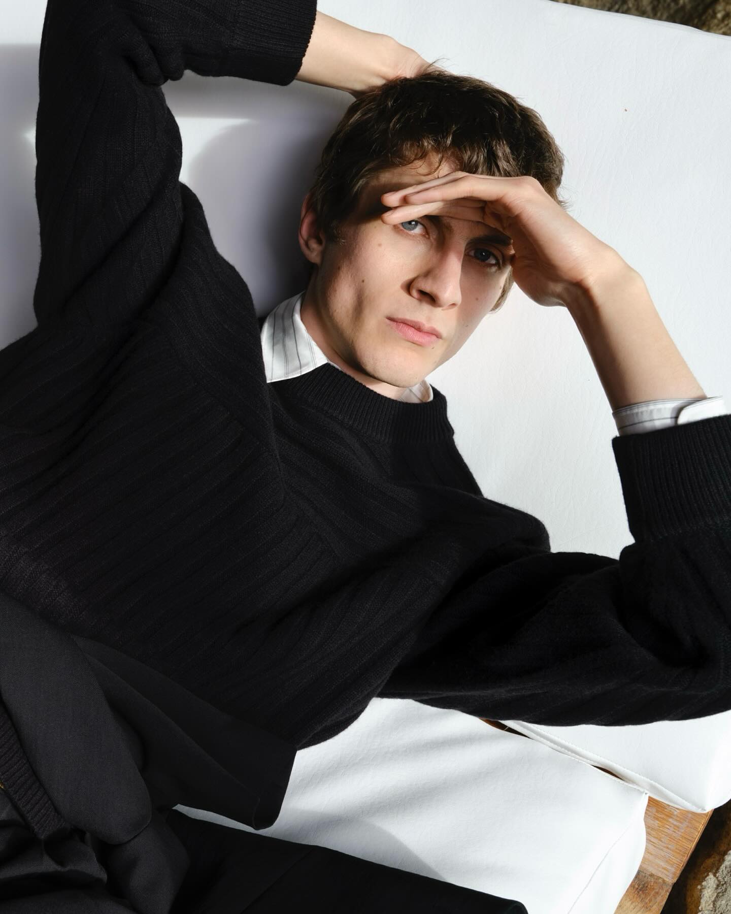 Model in black sweater with hands behind head against white background