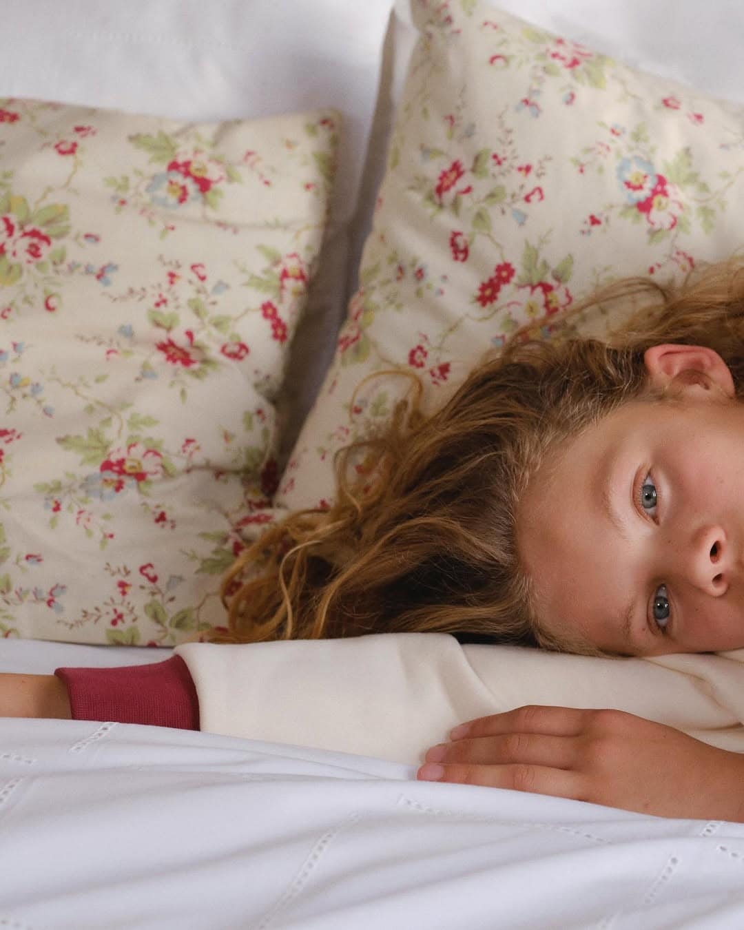 Close-up of a child resting head on floral pillows with a white blanket, photographed by Juliette Abitbol for Dior Kids.