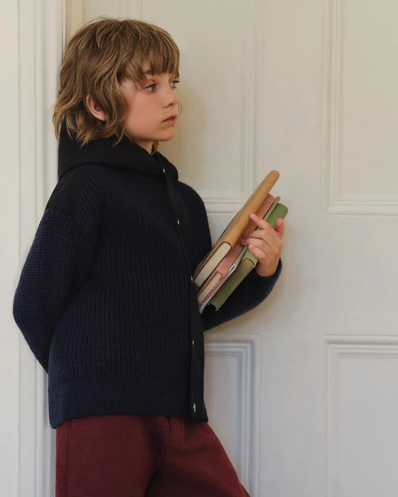 Young child holding a stack of books against a white paneled door for Dior Kids Spring 2025 ad campaign.