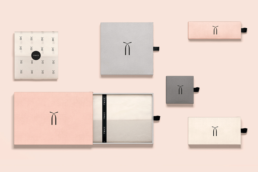 Flat lay of product packaging boxes and tissue paper in neutral and pink tones with a minimalist logo against a pale background