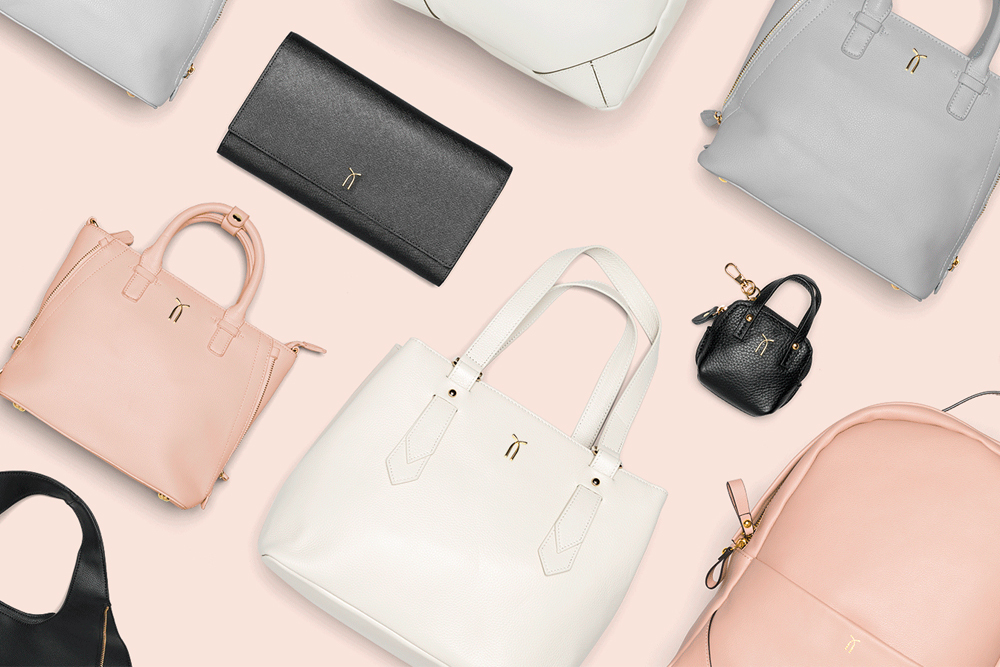 Flat lay arrangement of various leather handbags and accessories in pink, white, grey, and black on a neutral background.