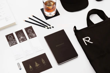 Overhead flat lay of Redscout brand identity collateral including a notebook, tote bag, pencils, cards, and a glass of whiskey.