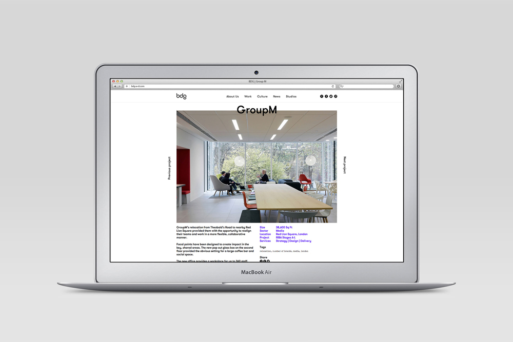 A silver laptop displaying the BDG brand identity website showcasing modern office interior design against a plain grey background