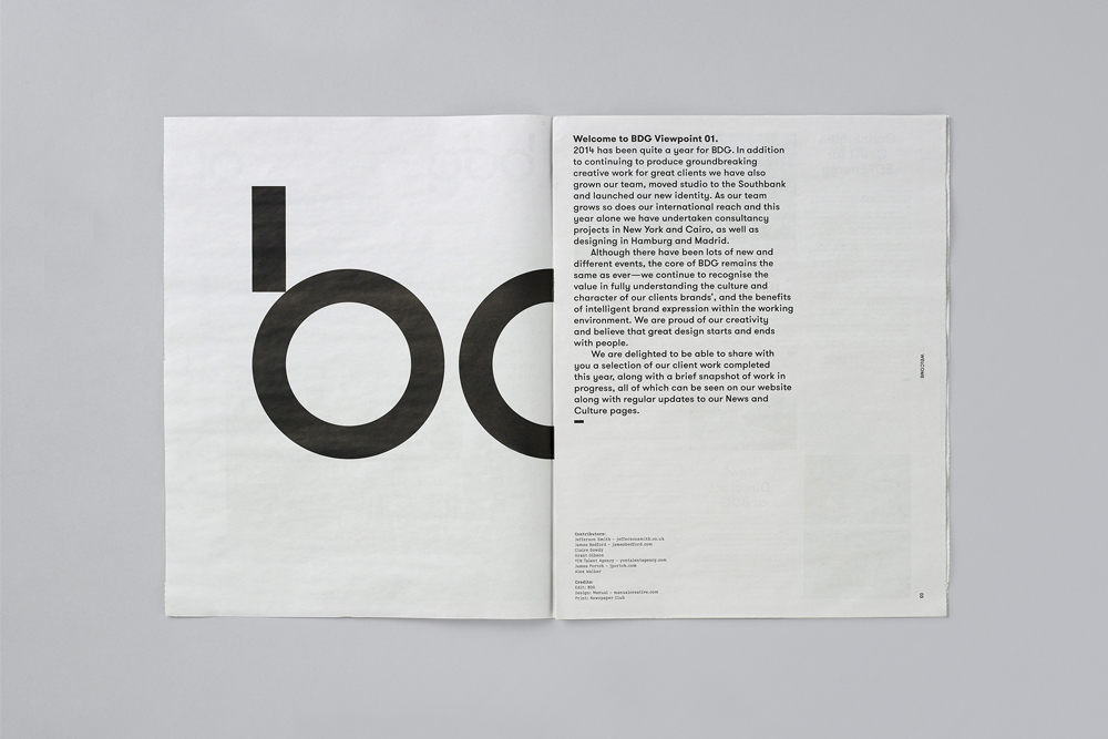 Open spread of a black and white print publication displaying bold typography and paragraphs of text on a grey surface.