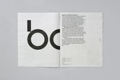 Open spread of a black and white print publication displaying bold typography and paragraphs of text on a grey surface.