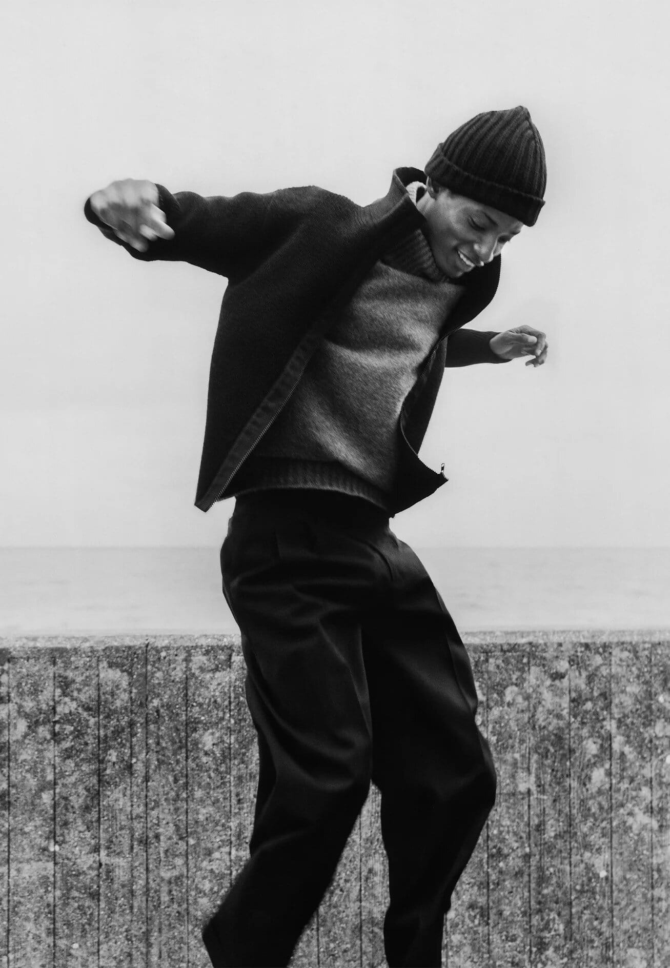 Monochrome portrait of a black man wearing a ribbed beanie and dark jacket outdoors against an open background