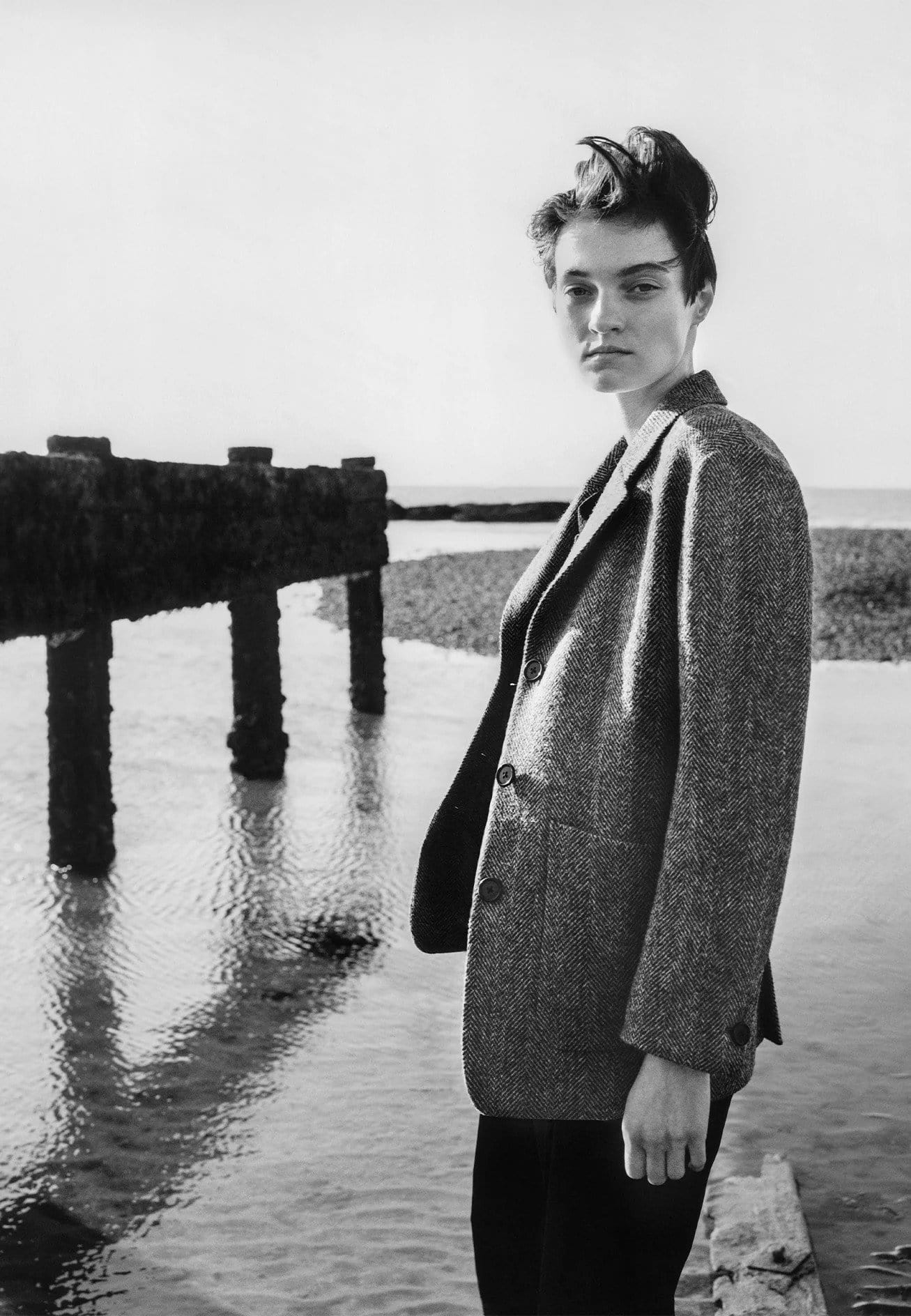Model standing on a coastline wearing a tweed blazer by Margaret Howell for the Fall 2025 ad campaign.