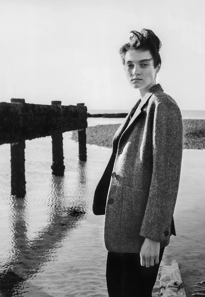 Model standing on a coastline wearing a tweed blazer by Margaret Howell for the Fall 2025 ad campaign.