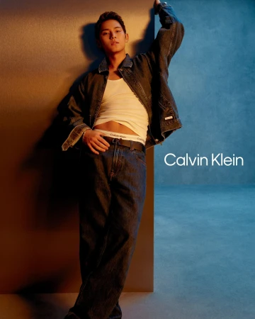 Man wearing a denim jacket and jeans leaning against a wall for a Calvin Klein denim campaign