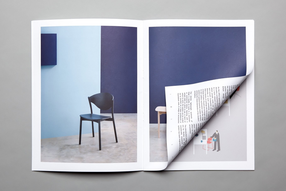 An open catalog displaying interior pages with a black chair and columns of text, resting on a flat grey surface.