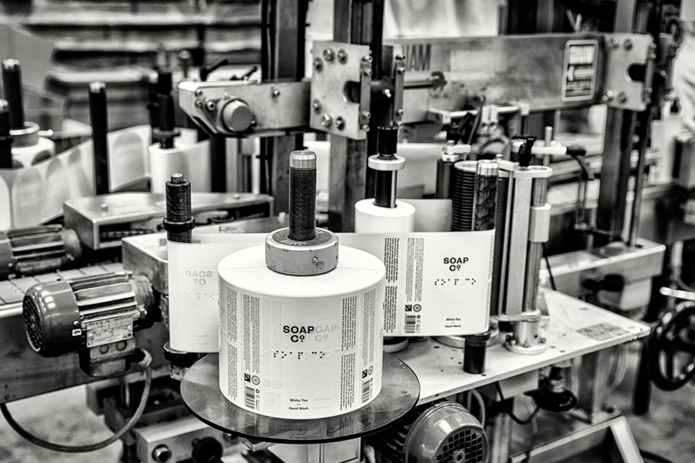 Monochrome industrial factory shot showing a label printing machine with rolls of labels for The Soap Co.