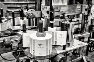 Monochrome industrial factory shot showing a label printing machine with rolls of labels for The Soap Co.