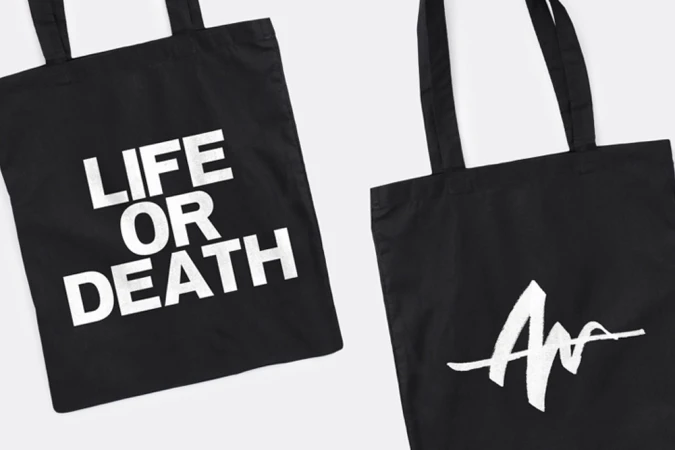 Two black cotton tote bags featuring bold white Life or Death typography and graphic logo prints on a clean background.