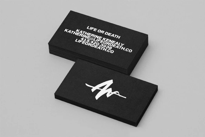 Black business cards for Life or Death with white typography and a graphic logo on a grey background