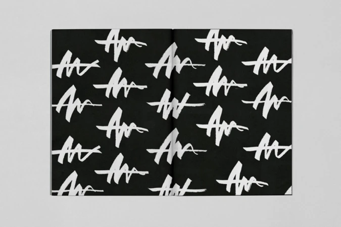 Open book layout featuring a repeating white brushstroke pattern on a black background set against a neutral grey surface.