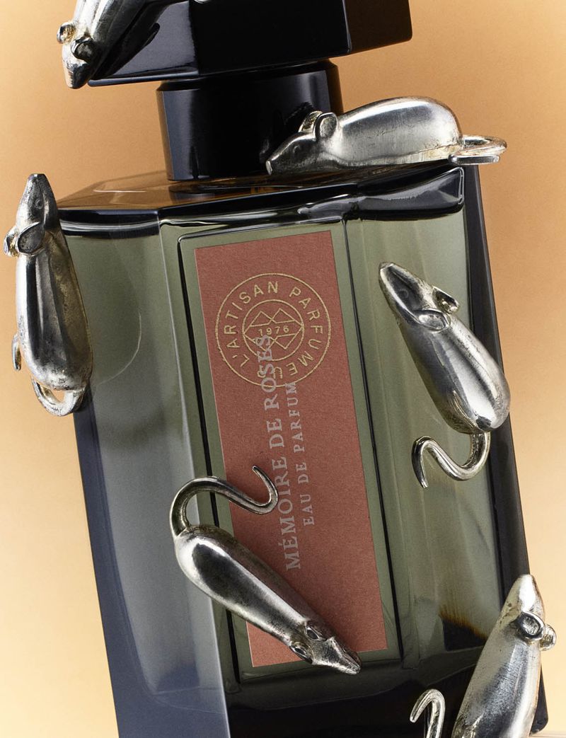 A bottle of grey glass perfume with a black stopper is embellished with several silver mouse figurines.