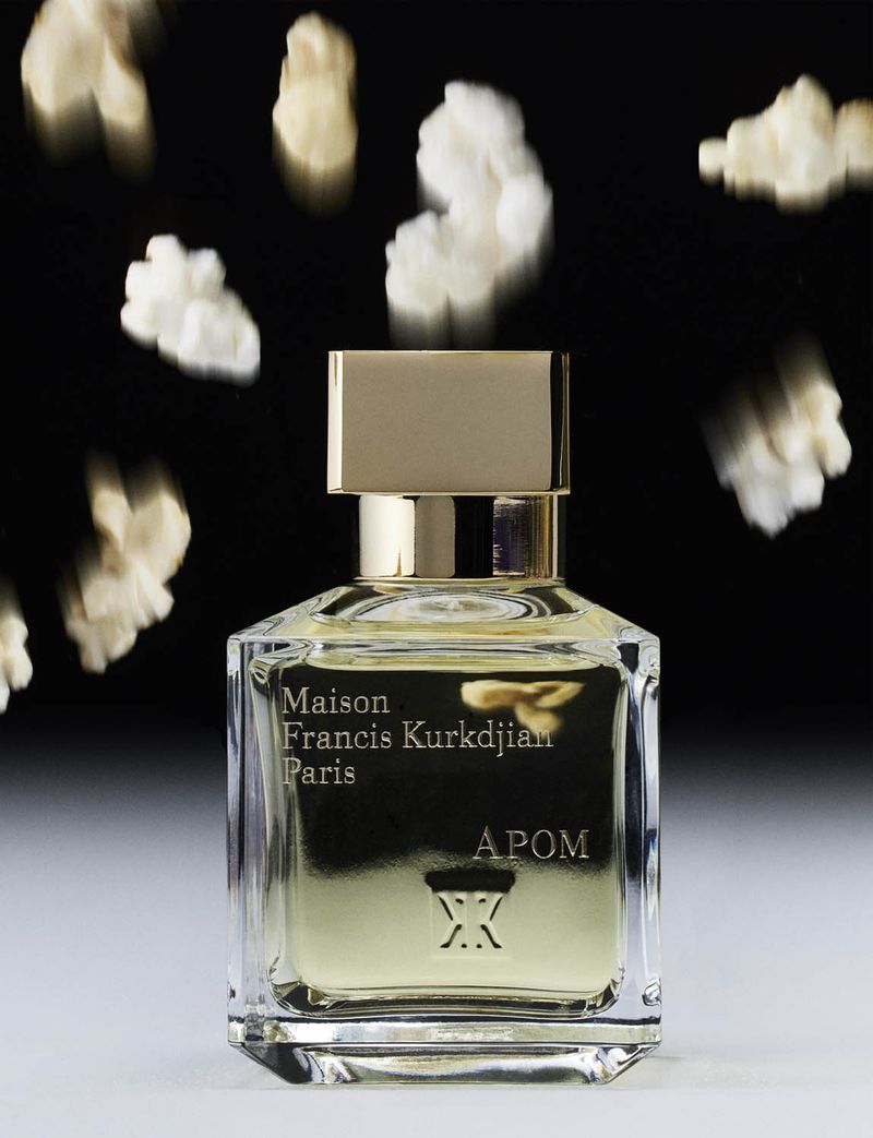 Elegant perfume bottle by Maison Francis Kurkdjian Paris on a white surface against a black background with blurred popcorn.