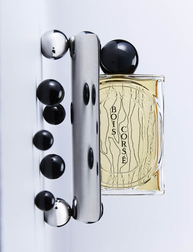 Eau de parfum by Bois Corsé, bottle with gold liquid and black and silver decorative accents, studio shot with white backdrop.