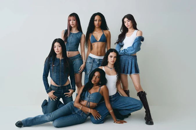 Group of six young female models wearing denim apparel and white tops posed against a neutral white seamless background.