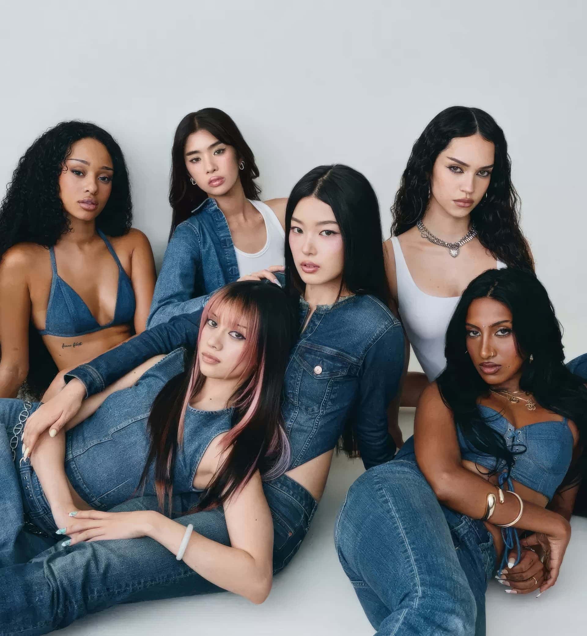 Group of six young women posing together in denim outfits against a clean white seamless studio background.