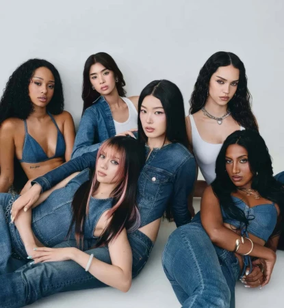 Group of six young women posing together in denim outfits against a clean white seamless studio background.