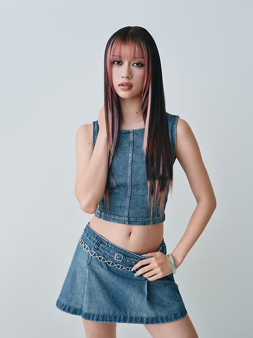 Young woman in a denim crop top and denim skirt posing against a light grey studio background.