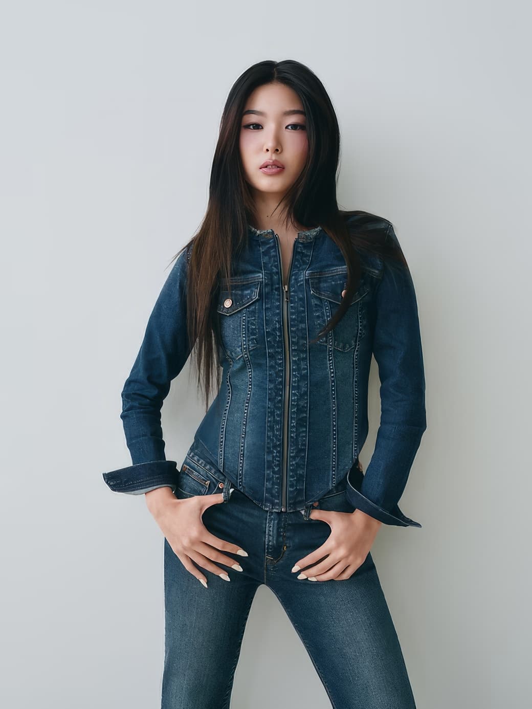 A young woman wearing a matching denim jacket and jeans posing against a plain neutral background.