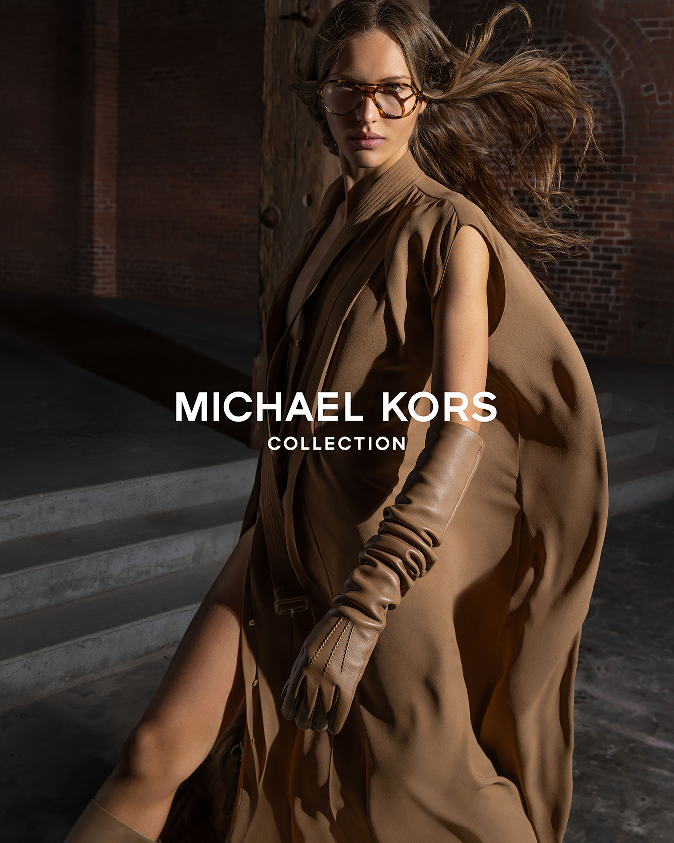 Model wearing brown cape dress and leather gloves with sunglasses in warehouse