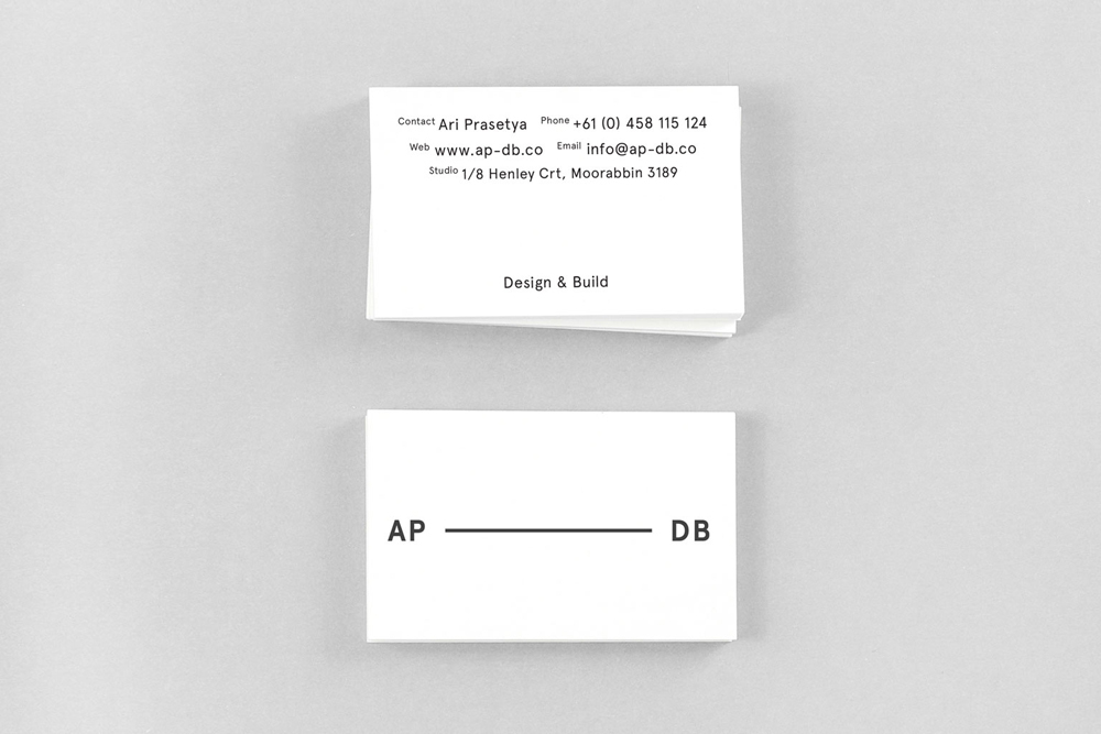 Two white business cards with minimalist black typography displayed on a neutral grey background.