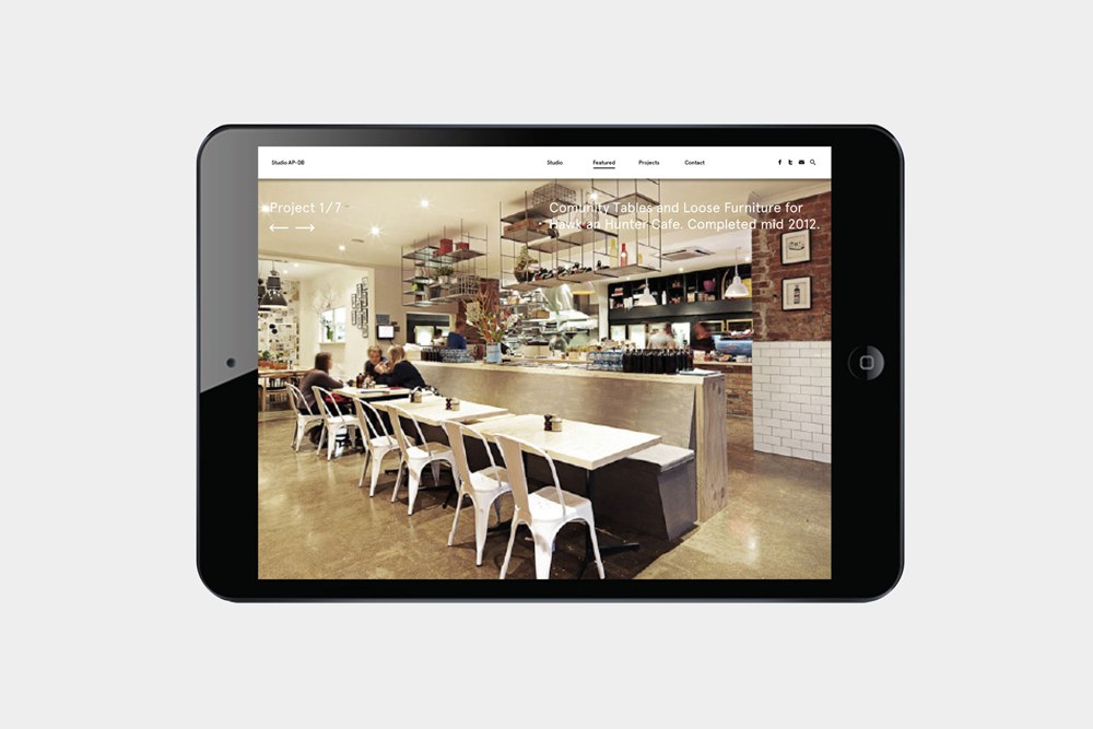A tablet device displaying a website featuring interior café design with wooden tables and white chairs.