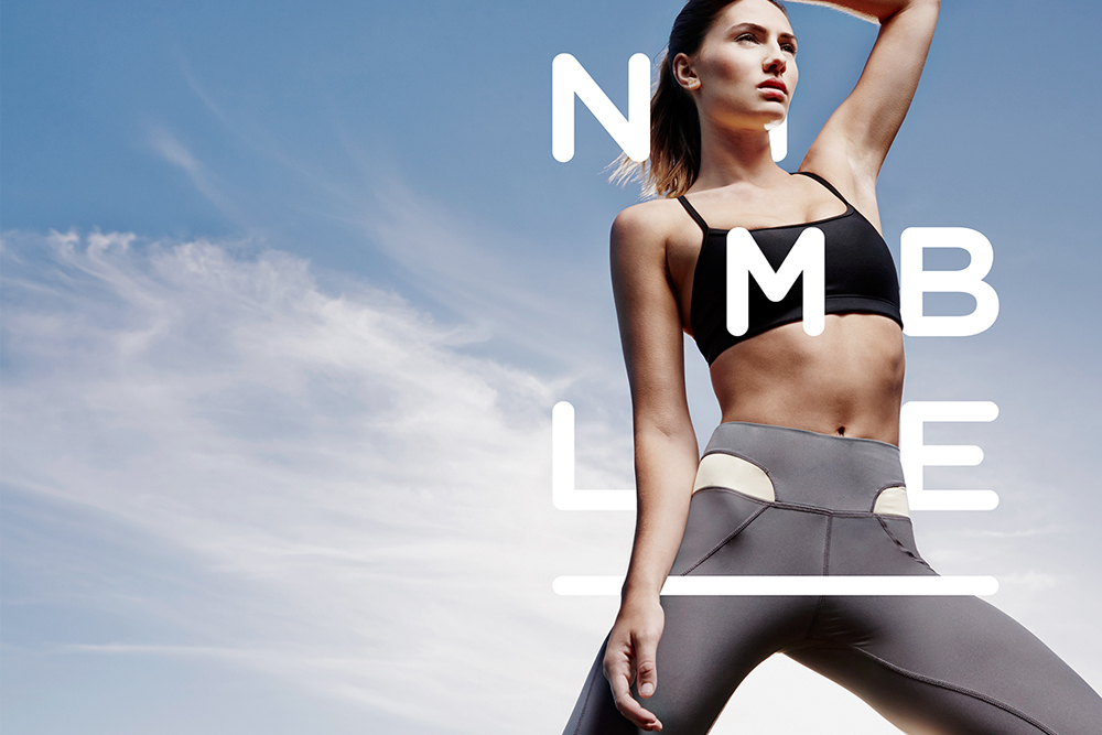 Woman in a black sports bra and grey activewear leggings posing against a clear blue sky background with large white typography.