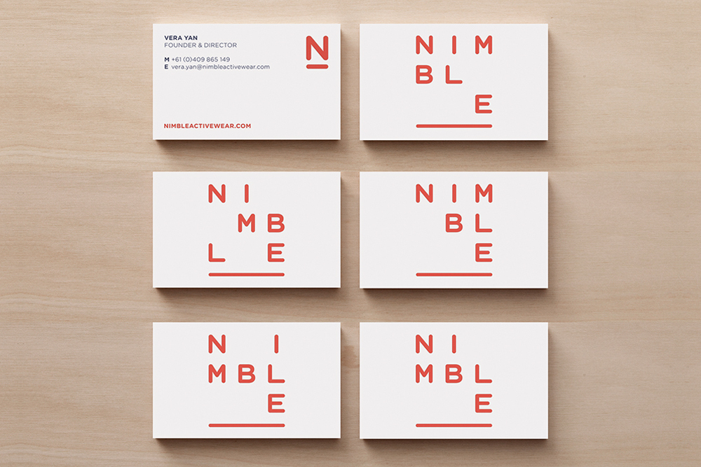 Six white business cards with red typography arranged neatly on a light wood grain surface.