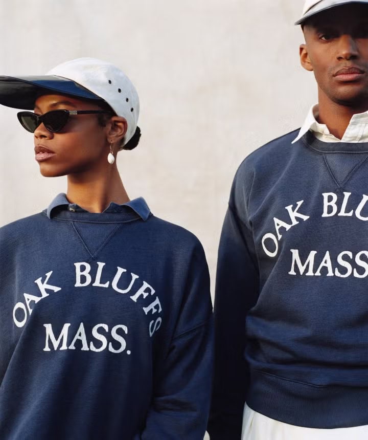 Two models wearing navy sweatshirts with 'OAK BLUFFS MASS.' lettering and white caps against a plain wall.