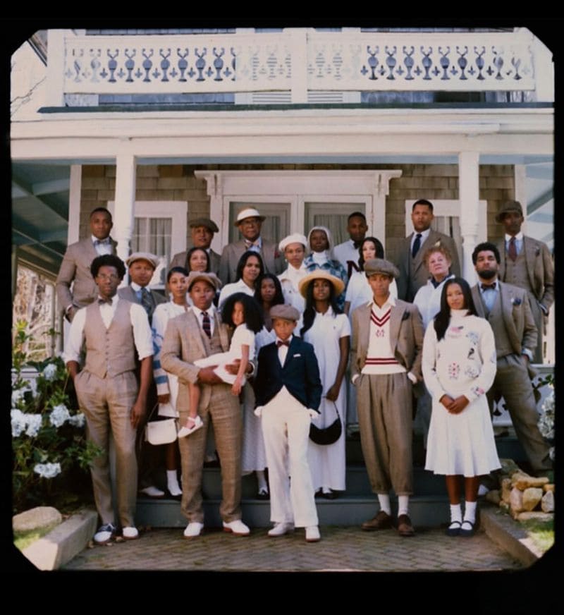 A large group of diverse models posing together on the porch of a classic two-story residential house for Polo Ralph Lauren.