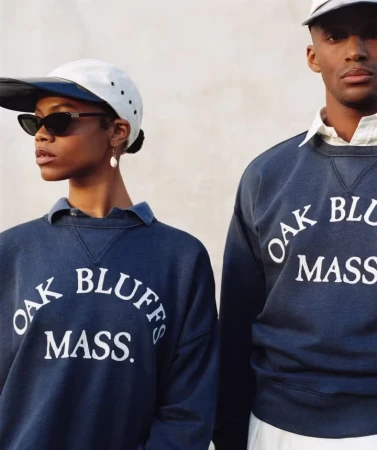 Two models wearing navy sweatshirts with 'OAK BLUFFS MASS.' lettering and white caps against a plain wall.