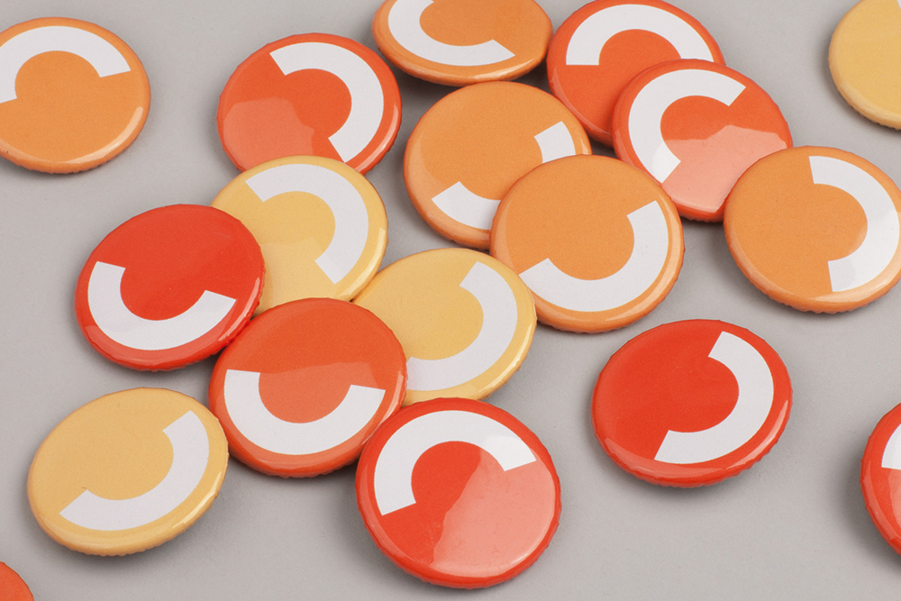 Collection of round orange, red, and yellow badges featuring white letter C graphic arranged on a grey surface.